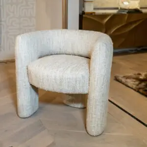 Close-up view of beige upholstered armchairs with rounded arms, standing on a light tiled floor in a living room.