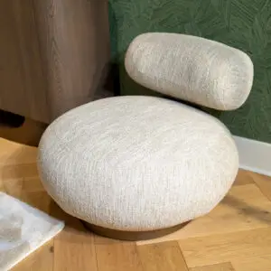Beige textured round ottomans stacked on a wooden floor with a green patterned wall behind them.
