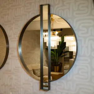 Decorative wall with interlocking circular mirrors and a vertical metal frame; chandelier and plant reflected in the glass.