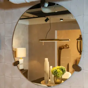 Curved wall mirror reflects a contemporary showroom with pendant lights and a vase of green hydrangeas on a wooden table, surrounded by candles.