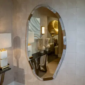 Oval wall mirror with a segmented metallic frame reflecting a gold sunburst decor and lamp in a boutique setting.