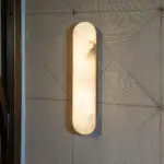 Vertical frosted glass wall sconce casting warm light on a textured wall with stacked chevron patterns.