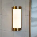 Brass-edged wall sconce with a frosted glass shade mounted on a textured padded wall.