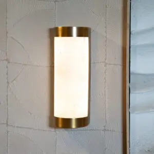 Brass-edged wall sconce with a frosted glass shade mounted on a textured padded wall.