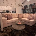 Beige sectional sofa with patterned throw pillows in a store display, round glass coffee tables, sale tags visible on tables and walls.