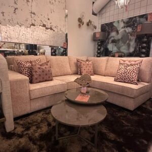 Beige sectional sofa with patterned throw pillows in a store display, round glass coffee tables, sale tags visible on tables and walls.