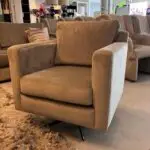 Beige upholstered armchair with straight arms and a back cushion in a furniture showroom.