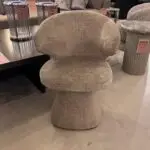 Beige sculptural chair with a thick curved back and pedestal base in a showroom, surrounded by sale-tagged display furniture.
