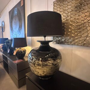 Showroom display with a glossy black ceramic lamp on a dark console against a stone-tile wall.