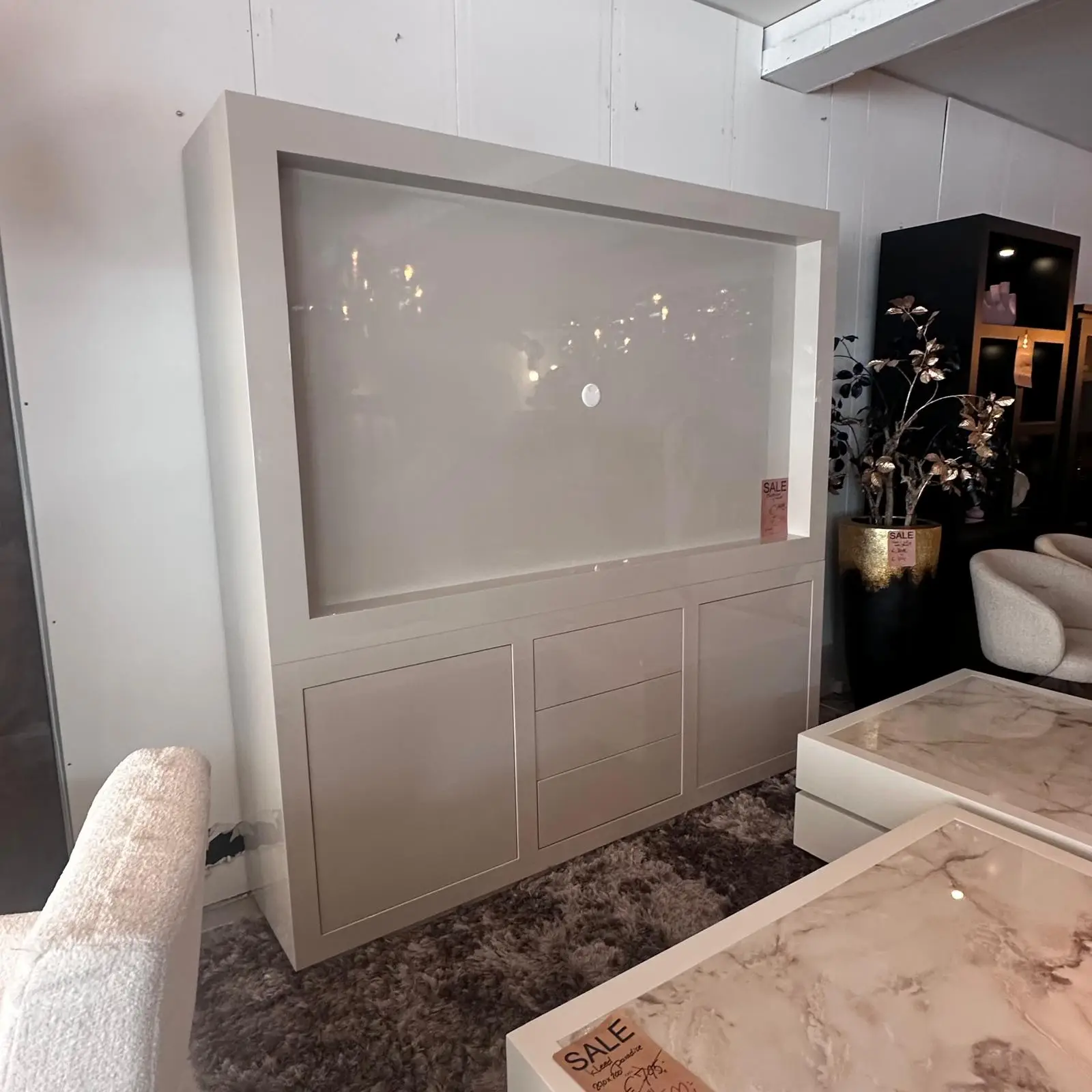 Large beige built-in display cabinet with frosted glass door and lower drawers, showroom setting with sale tag nearby