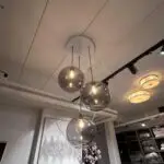 Cluster of clear glass pendant lights hanging from a white ceiling, bulbs glowing inside each globe in a showroom.