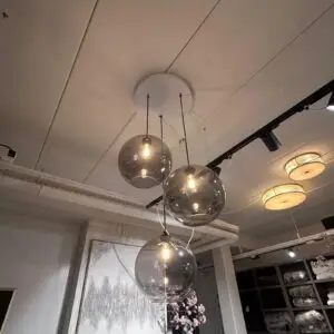 Cluster of clear glass pendant lights hanging from a white ceiling, bulbs glowing inside each globe in a showroom.
