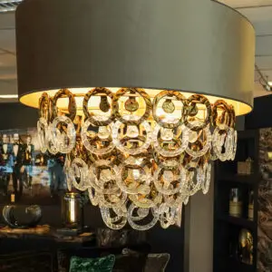 Luxurious chandelier with gold and crystal circular rings hanging under a large drum shade, lit in a showroom setting.