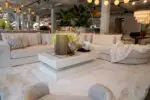Neutral showroom living room with light beige sectional sofa, plush cushions, and a white shag rug displaying modern decor on a white coffee table.