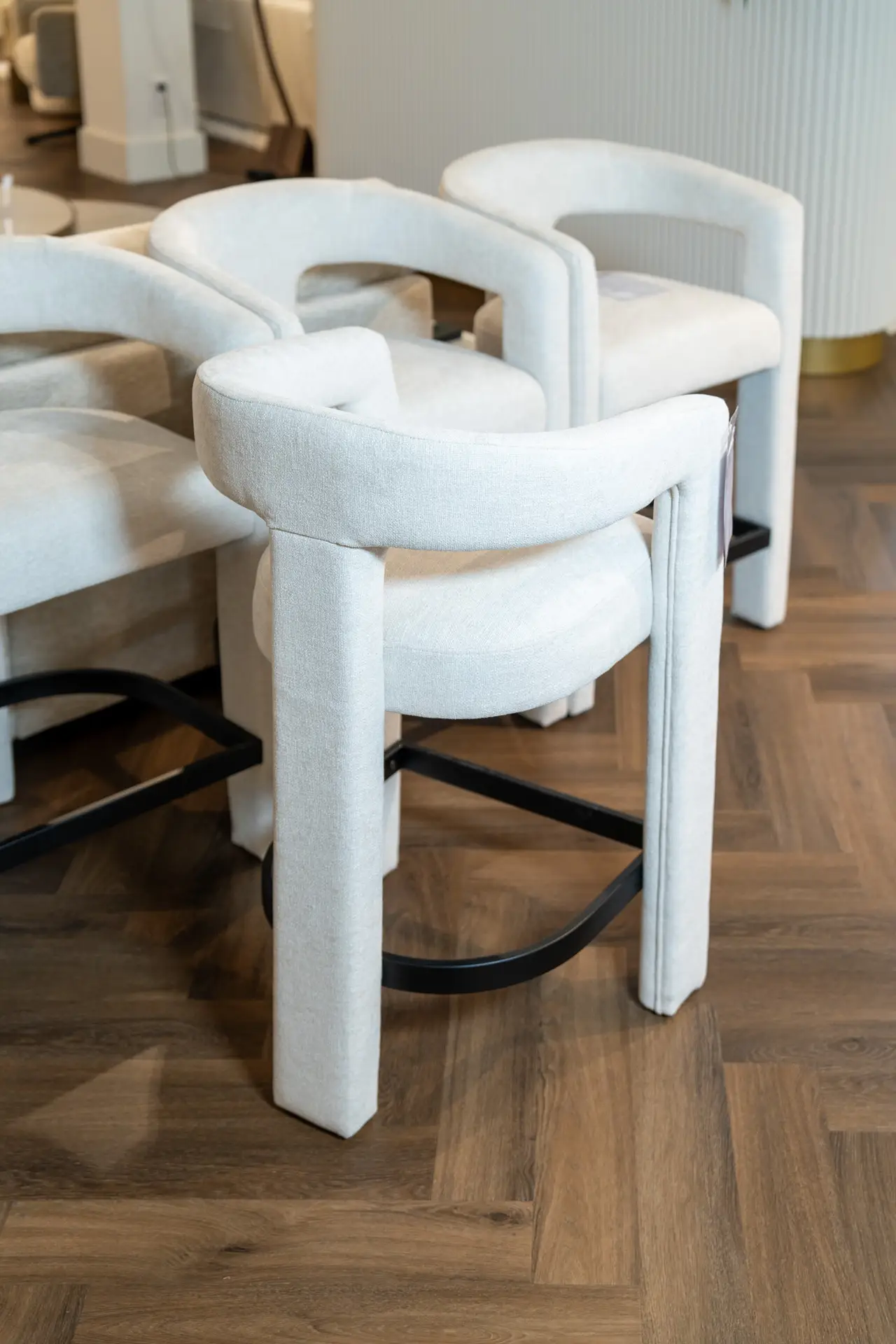 Row of light beige upholstered chairs with curved arms on a wooden floor in a showroom setting.