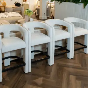 Row of light beige upholstered chairs with black metal bases in a furniture showroom, with sofas and plants in the background.