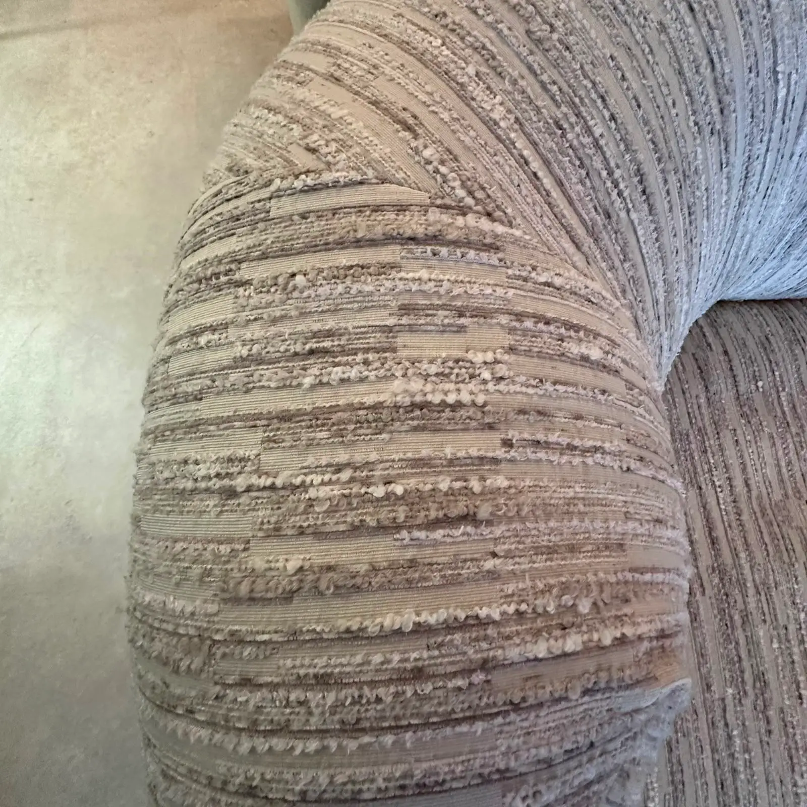 Close-up of a beige upholstered sofa arm with textured horizontal stripes and looped fringe detail