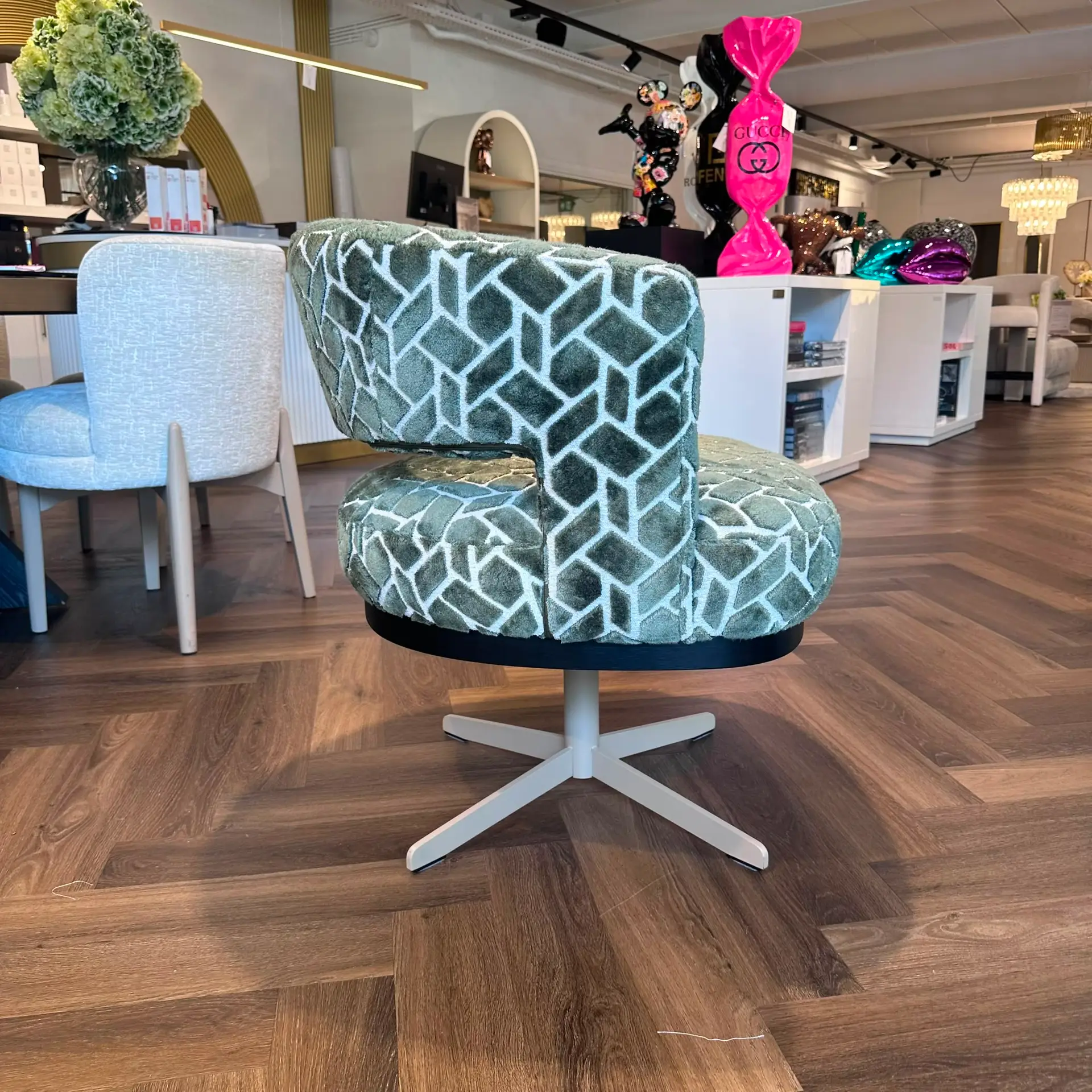Turquoise patterned ottomans stacked on a pedestal in a furniture showroom, with a green hydrangea bouquet and decorative items in the background