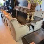 Showroom seating: beige tufted sofas along a glass‑top table, with a large amber vase and hanging sale signs.