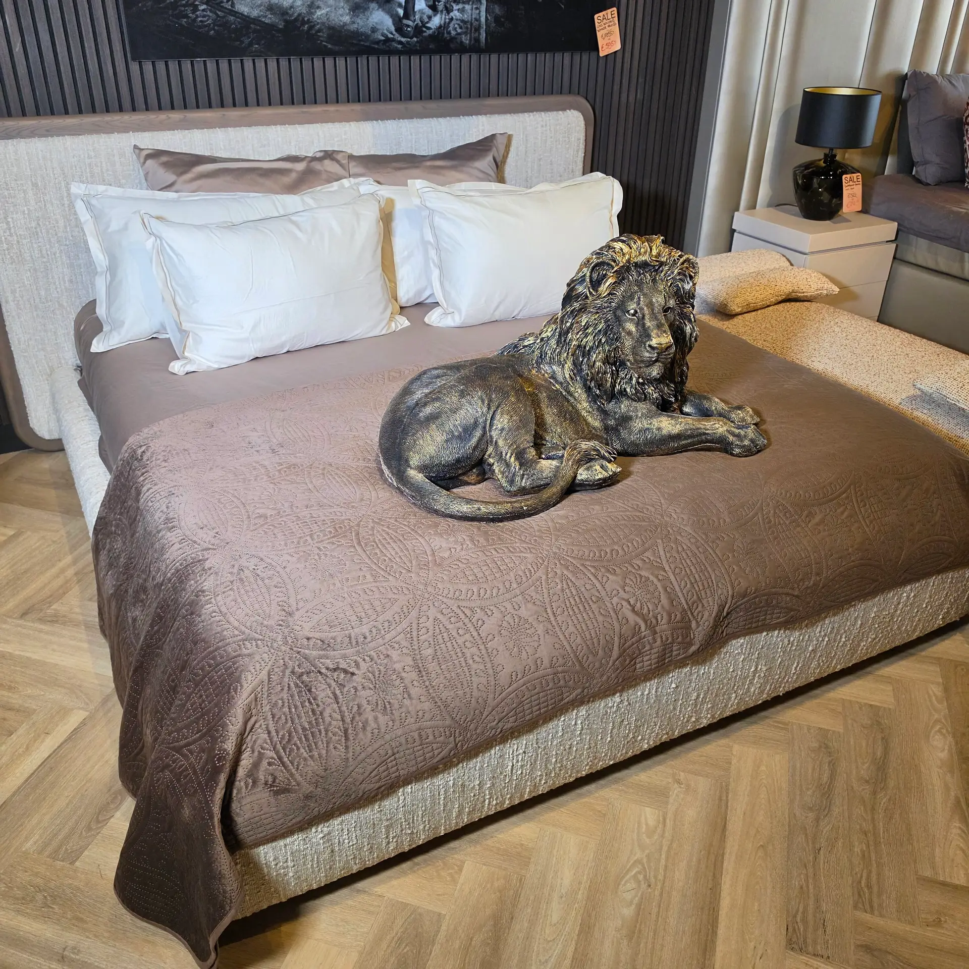 Bedroom scene with a brown quilted bedspread, white pillows, and a bronze dog statue resting on the duvet.