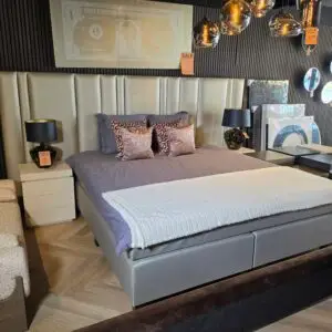 Bedroom display: large grey upholstered bed with matching nightstands, grey bedding, and patterned throw pillows with sale tags visible.