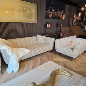 Showroom living room setup with beige textured sofas, a white plush throw, and a large gold snake sculpture on a marble coffee table.