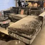 Velvety gray sectional sofa set in a showroom with multiple cushions and a sales tag tucked on the middle cushion.