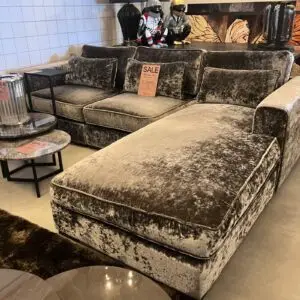 Velvety gray sectional sofa set in a showroom with multiple cushions and a sales tag tucked on the middle cushion.