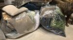 Pile of cushions and pillows wrapped in plastic, stored under a dark sofa.