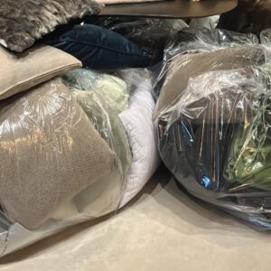 Pile of cushions and pillows wrapped in plastic, stored under a dark sofa.