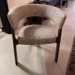 Curved-back upholstered chair with beige geometric fabric and dark wooden legs in a showroom setting.