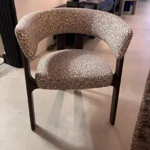 Curved-back upholstered chair with beige geometric fabric and dark wooden legs in a showroom setting.