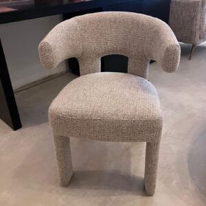 Beige boucle chair with a curved back and short legs, shown in a showroom setting.