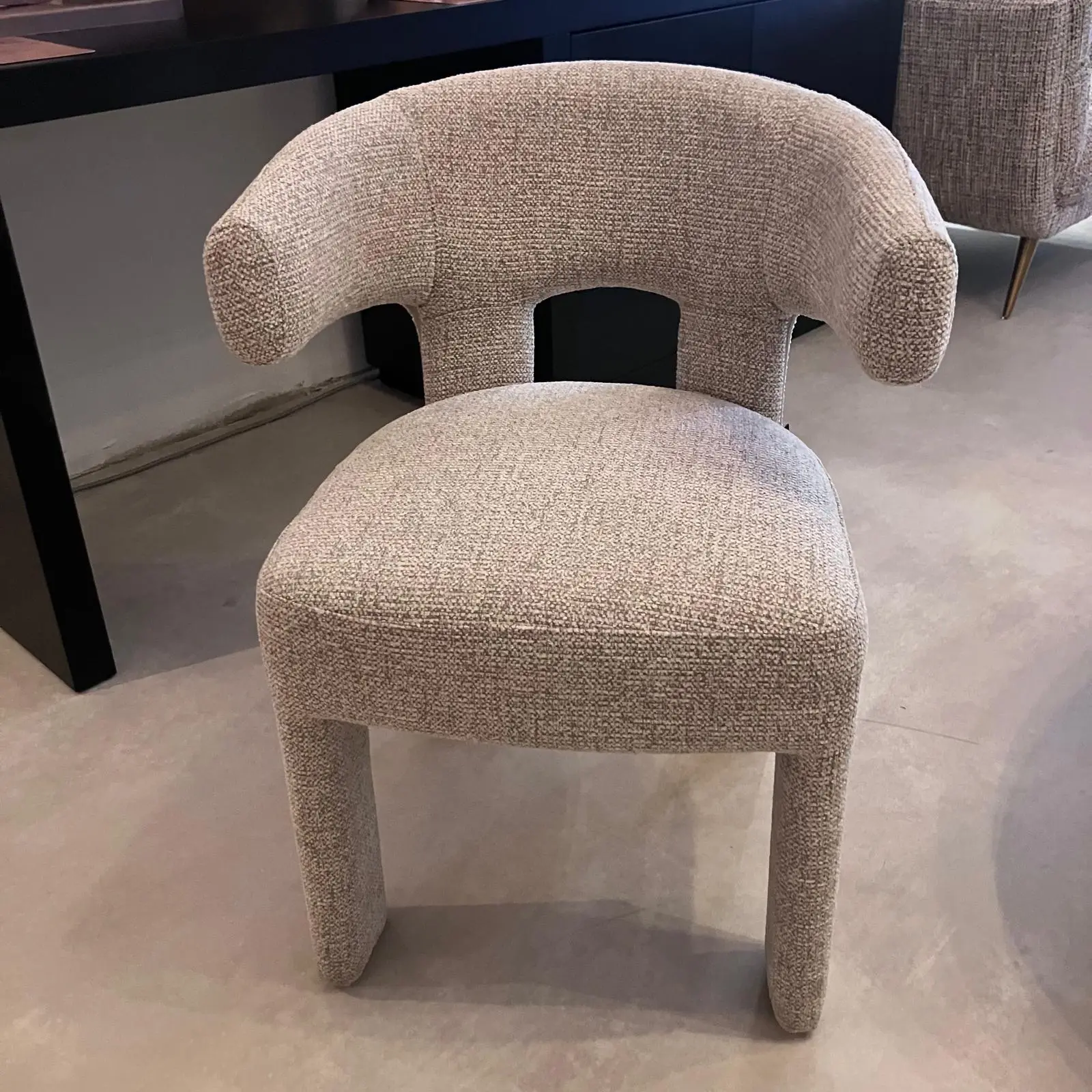 Beige boucle chair with a curved back and short legs, shown in a showroom setting.