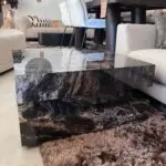 Stacked black marble coffee tables with glossy surfaces in a furniture showroom, reflecting nearby chairs and decor.