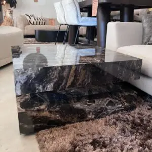 Stacked black marble coffee tables with glossy surfaces in a furniture showroom, reflecting nearby chairs and decor.