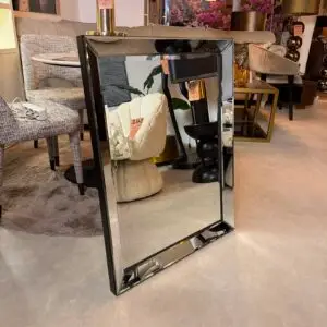 Full-length rectangular mirror with beveled edges on a black stand in a furniture showroom, reflecting beige chairs and pink flowers; sale tag visible.